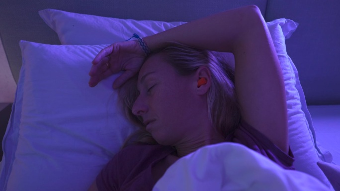 疲惫的女人躺在床上，戴着耳塞，想睡个好觉