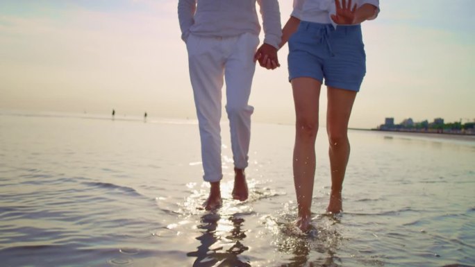 男女手牵着手赤脚走在沙滩上