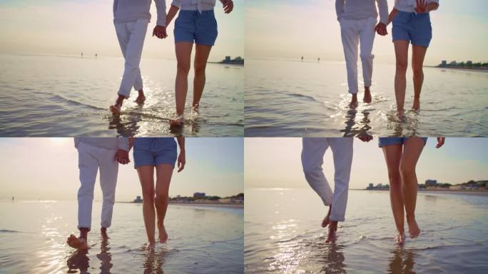 男女手牵着手赤脚走在沙滩上