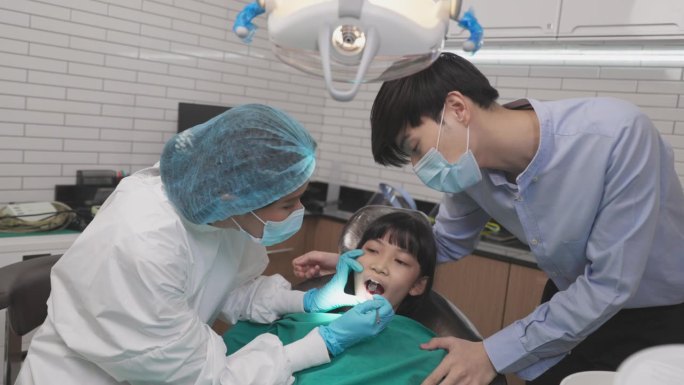 女牙医在牙科诊所拿着牙齿模型和孩子说话。