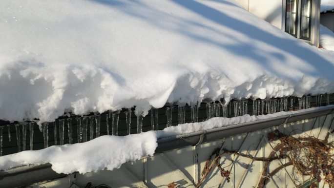 冰柱从积雪的屋顶垂到阴沟里