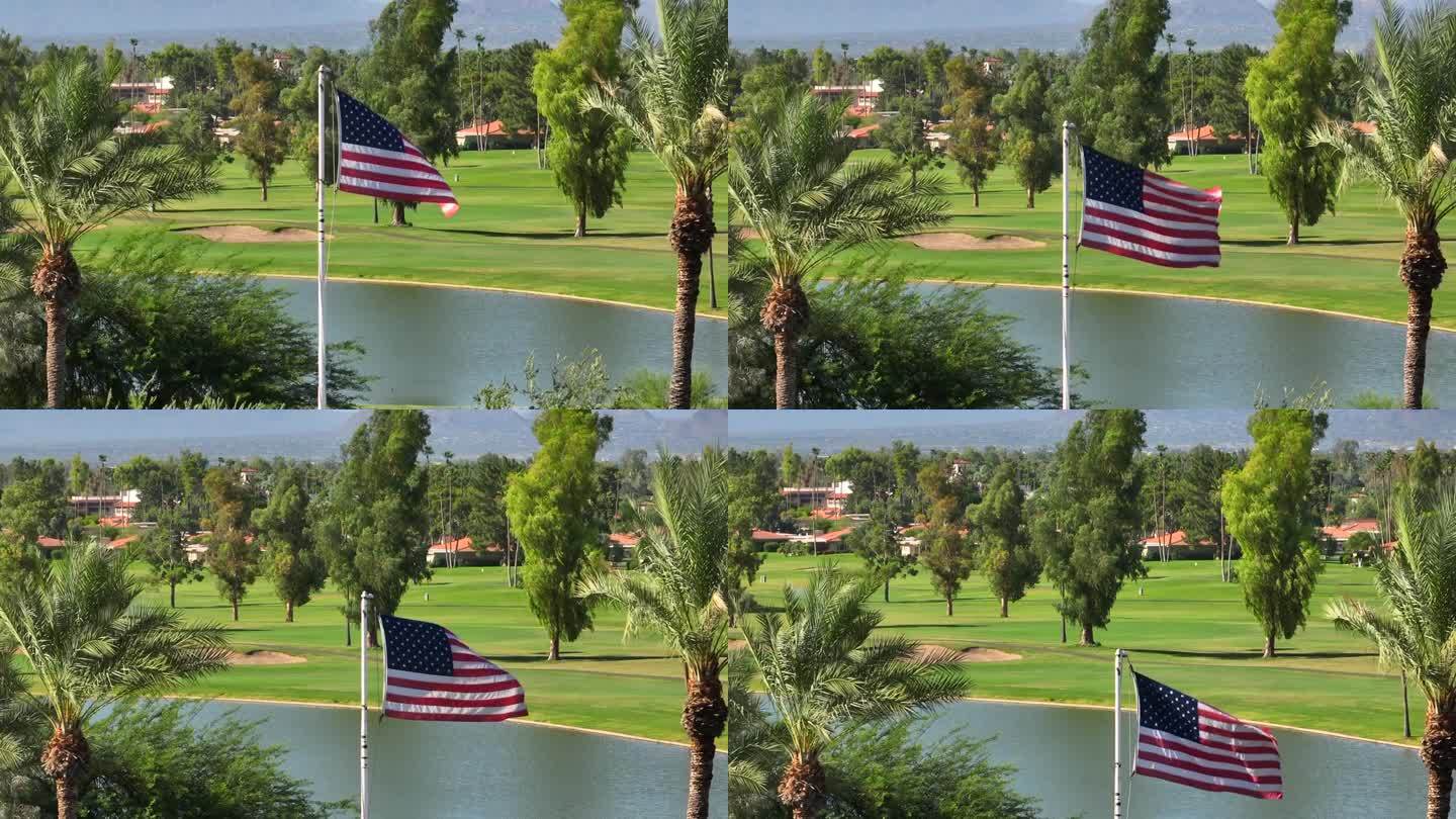 美国西南部棕榈树丛生的豪华乡村俱乐部高尔夫球场前飘扬的美国国旗。空中上升的照片显示湖泊和果岭。