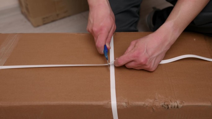 一个人，一个家具装配工，用一把文书刀打开一个纸板箱。打开盒子的概念。特写镜头