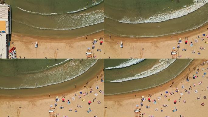 无人机从上到下拍摄了一个熙熙攘攘的海滩，充满了热情的游泳者和日光浴家庭，在暑假期间创造了难忘的回忆