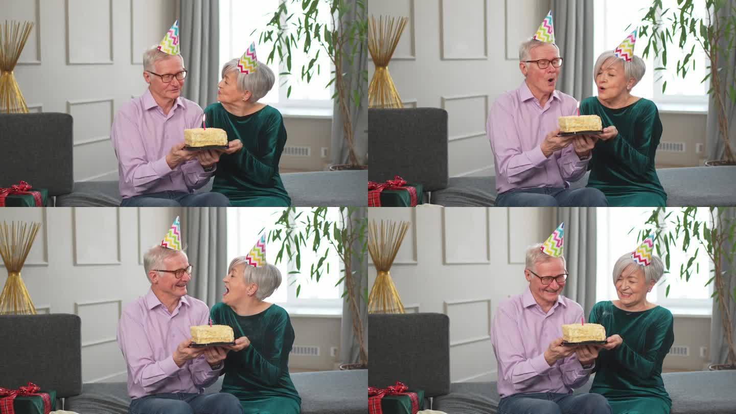 许个愿。家庭高级夫妇戴着派对帽在家里一起庆祝生日纪念日。老人吹灭了生日蛋糕上燃烧的蜡烛。老太太祝丈夫