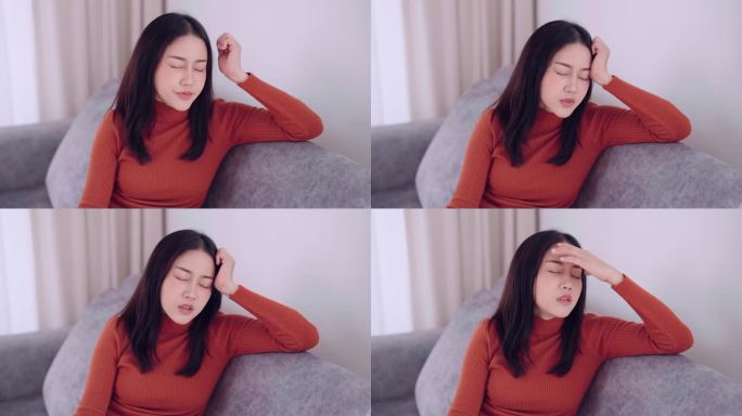 一名亚洲女性坐在家里的沙发上，因为焦虑而感到压力和头痛
