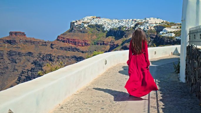 一个穿着红裙子的美丽女孩走在圣托里尼，参观欧洲著名的旅游景点。