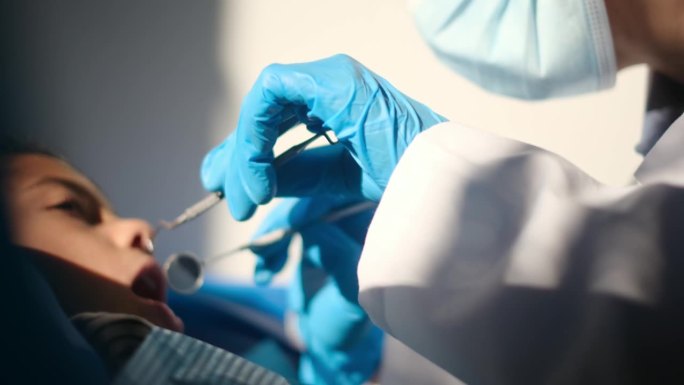 一位善良的女牙医用牙探针和角度镜为一位年轻病人检查蛀牙