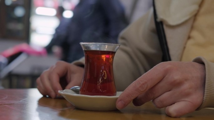 一名妇女在街边的咖啡馆里喝着国家杯的红茶。女性用手用茶匙搅拌热饮。