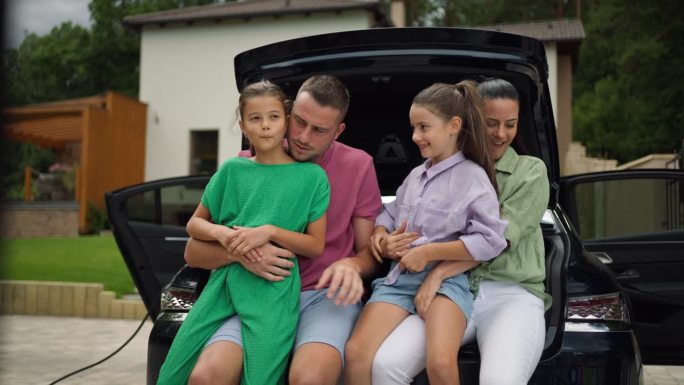 一家人坐在打开的汽车后备箱里，面带微笑。