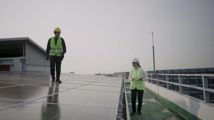 团队承包商，男技术人员和女工程师穿着安全制服，谈论安装方案，检查工作系统和维护太阳能发电厂的太阳能电