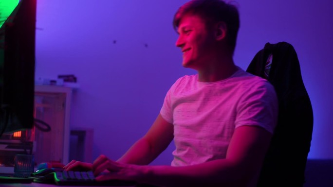 特写:开朗的年轻人在网上玩电脑视频游戏，五彩缤纷的灯光在家里直播。欣喜若狂地庆祝胜利。