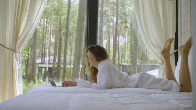 女人躺在床上用笔记本电脑，打字，微笑，大笑，发短信，交流，聊天