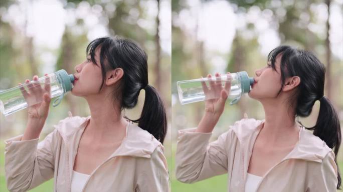 一名穿着运动服的亚洲女性在公园运动结束后，正在喝水。在户外健身过程中展示水合作用和健康，以获得清爽的