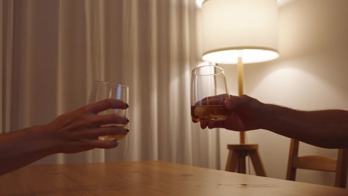 在一盏灯和浪漫柔和的灯光的映照下，一个女人和一个男人的手拿着威士忌酒杯走近，把他们碰在一起。