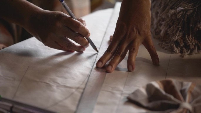 女裁缝正在用钢尺和铅笔在纸上画出要缝的图案。