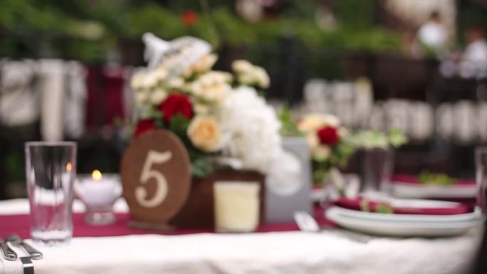 优雅的户外婚礼台面与花卉安排。红白颜色的主题，编号的中心，餐桌设置庆祝活动。理想的镜头浪漫的场合，活