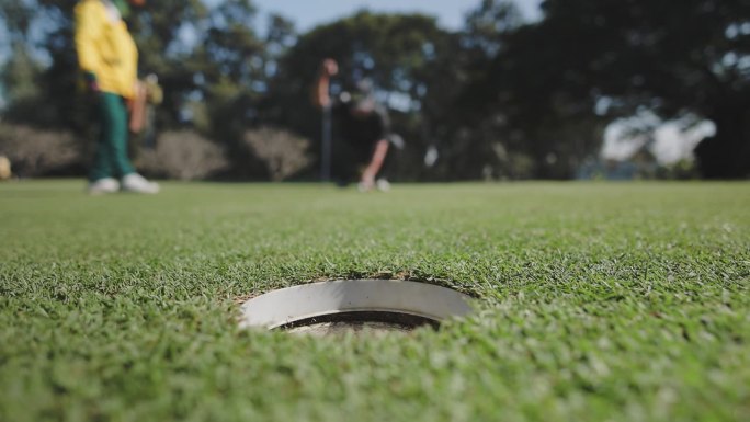 熟练的高尔夫球手将球打入果岭上的球洞