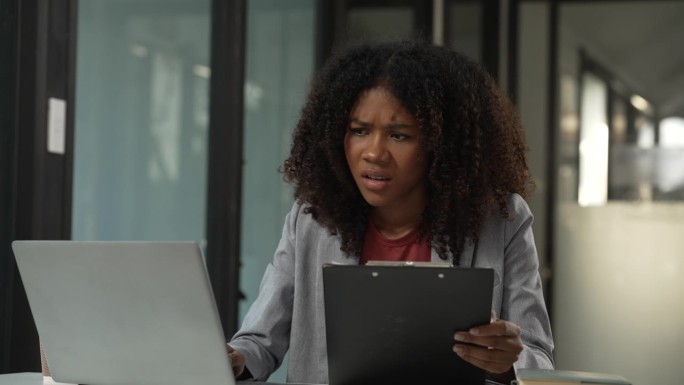 一名留着非洲式发型的美籍黑人女性，神情紧张，一只手放在额头上，看着一台笔记本电脑。