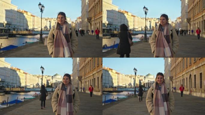 微笑的年轻女子，穿着时髦的长外套，走在里雅斯特的运河和城市建筑旁