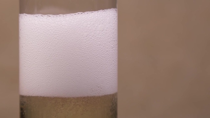 在玻璃杯中装满碳酸饮料，并在其表面形成白色泡沫。