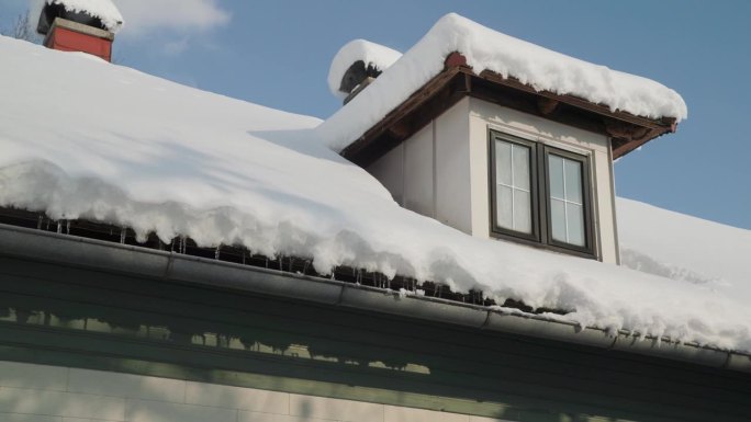 阴沟里的冰柱和带天窗的被雪覆盖的屋顶