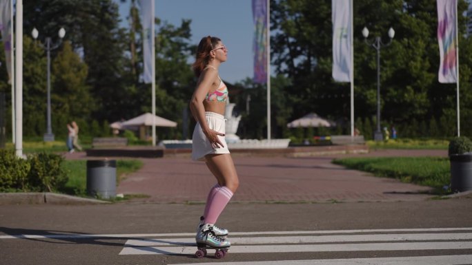 在一个阳光明媚的日子里，一位戴着眼镜的美丽女子在城市公园的户外背景下穿着溜冰鞋优雅地移动。缓慢的运动