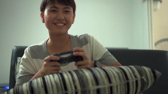 亚洲年轻女孩拿着摇杆在家里的沙发上玩电子游戏。