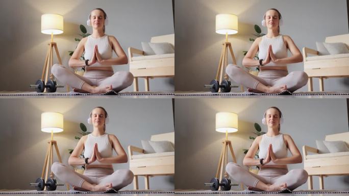 放松和健康的音乐。在辛苦的一周后，戴着耳机的女人在家地板上听教程冥想做瑜伽，让手掌保持祈祷的姿势放松