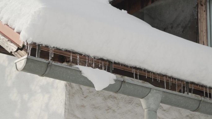 阴沟里的冰柱和被雪覆盖的屋顶