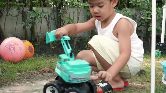 一个男孩在一堆沙子上玩玩具拖拉机。
