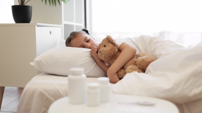 可爱的生病女孩在家里和泰迪熊睡得很香