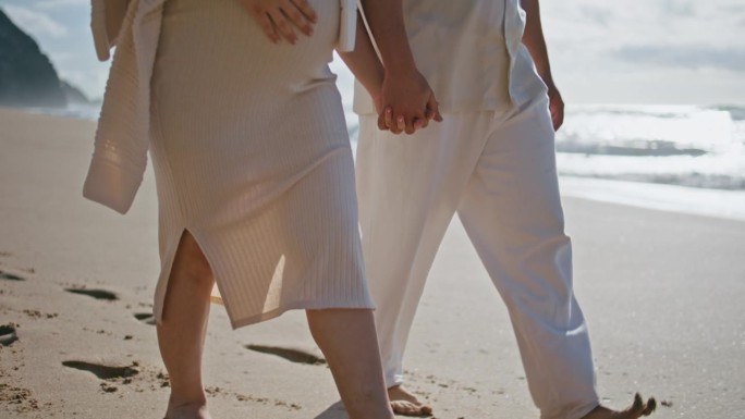 一对腿走在海滩附近的海浪特写。怀孕夫妇在海上休闲