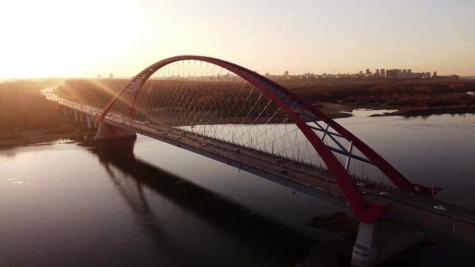 一座横跨这条河的红色大桥。Autobili沿着道路移动，在阳光下留下长长的影子。