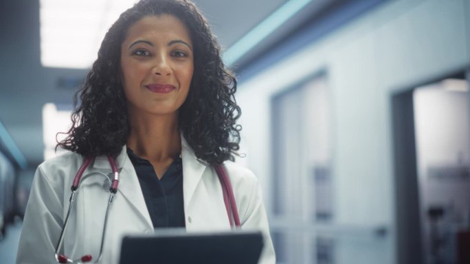穿白大褂的女医生在医院走廊用平板电脑工作的画像。医疗保健专业人员或护士长看着镜头，温柔地微笑。慢动作