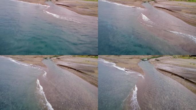 无人机捕捉到小溪蜿蜒穿过海滩，在日落时分与大海相遇。克里克从沙滩到大海的鸟瞰图。小溪流过沙滩，汇入大