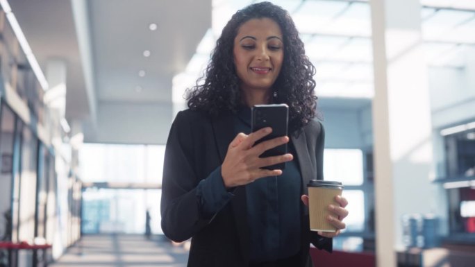 一个快乐的多民族女性的肖像，她在智能手机上发短信，走在公司办公室里。自信的女性营销经理查看社交媒体趋