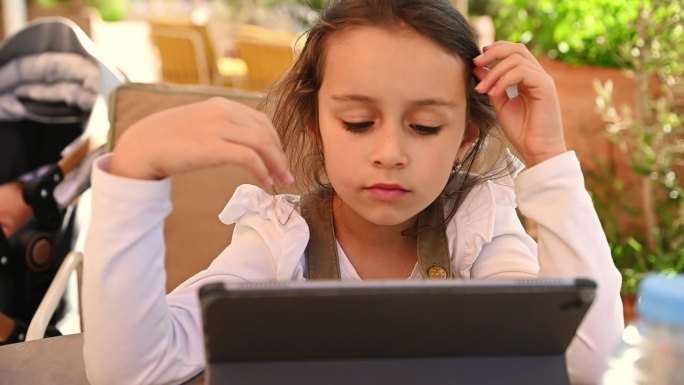 可爱的小女孩使用数码平板电脑，在户外做在线作业