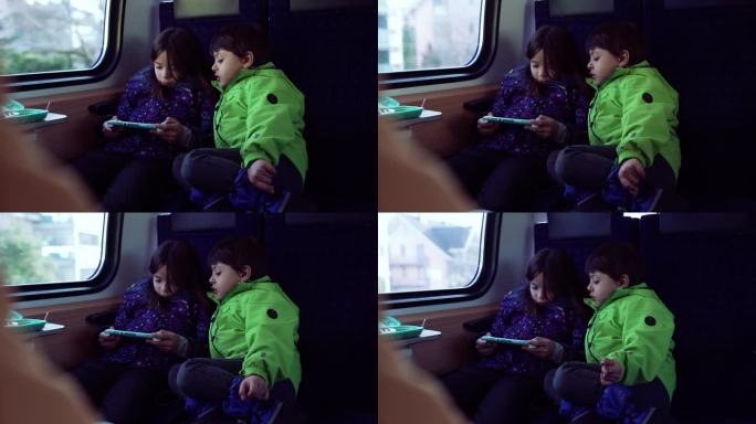 乘客小女孩拿着掌上游戏机玩游戏，弟弟盯着她的屏幕玩，孩子们在火车里玩科技