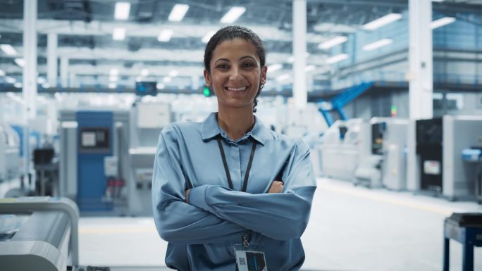 西班牙裔女性设施经理的肖像，双臂交叉，看着镜头，微笑着。工业专家在一家自主电子工厂工作，生产现代计算