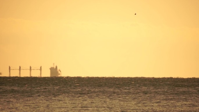 地平线上出现了货船的幻影。船在海上航行。温暖的金色水面上的小波浪和来自太阳的散景灯光。大海、大自然和