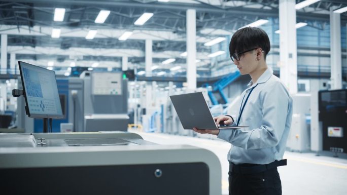 亚洲男工程师在电子厂用笔记本电脑控制焊锡喷墨打印机。为人工智能系统生产创新印刷电路板的人。