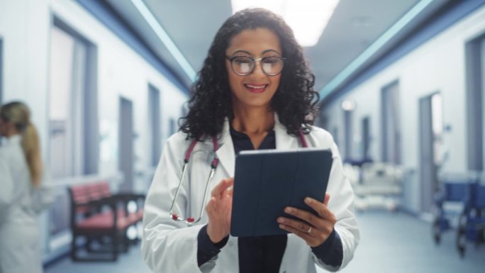 医院:专业多民族女医师边走边用数码平板电脑。穿着白大褂的医生开着药，准备拯救生命