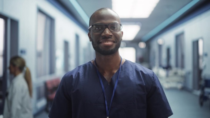 一个黑人医疗保健专业人员的肖像，对着相机摆姿势，微笑着看着相机。戴眼镜在医院办公室工作的临床医师或护