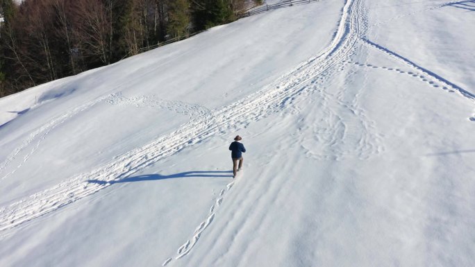 年轻的成年男子，穿着牛仔夹克，戴着帽子，在冬天的雪山上行走奔跑