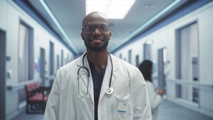 一个黑人医疗保健专业人员的肖像，对着相机摆姿势，微笑着看着相机。戴眼镜穿白大褂在医院办公室工作的门诊
