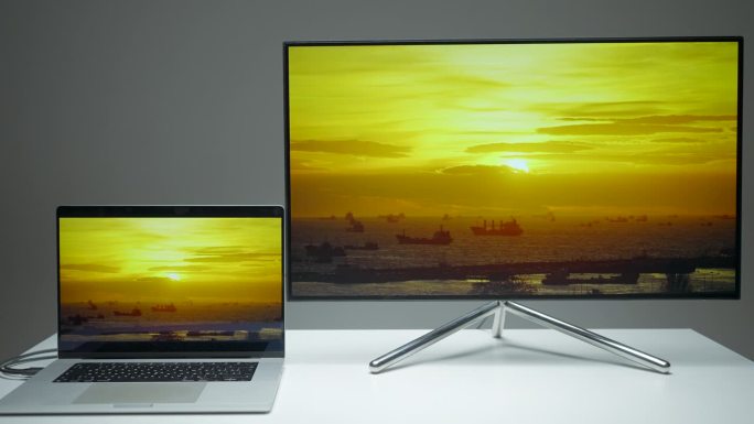 笔记本电脑通过hdmi在电视屏幕上传输图像。行动。电脑和新电视放在桌子上，背景是灰色的墙