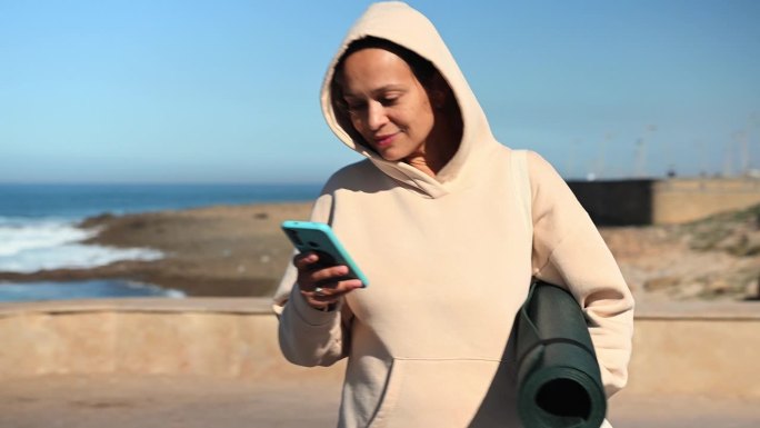 快乐的多民族年轻成年妇女使用智能手机，站在大西洋的海岸线上