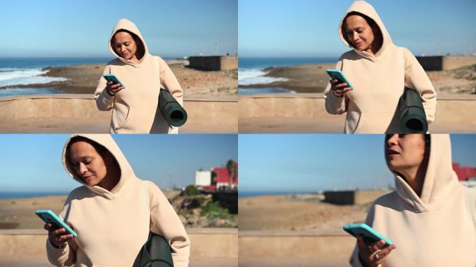 快乐的多民族年轻成年妇女使用智能手机，站在大西洋的海岸线上