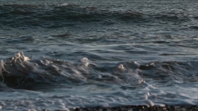 海上慢浪的特写。有创造力。美丽的波浪在石头岸边的慢动作。日落时美丽的海浪的石滩。